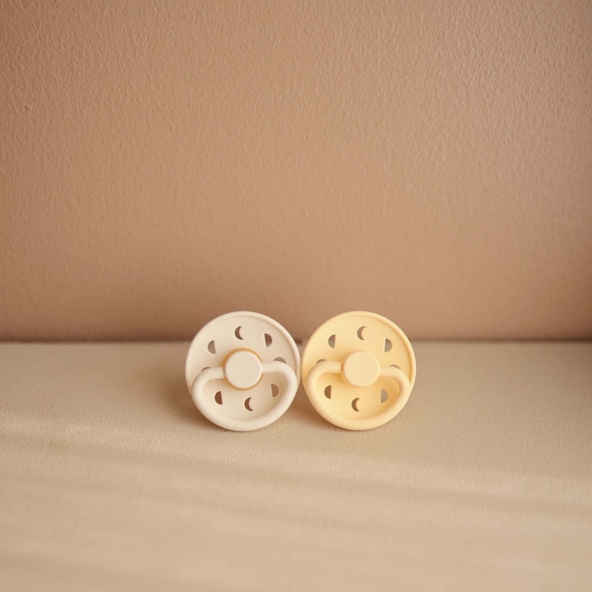 Lifestyle image of the Cream and Pale Daffodil Moon Silicone Frigg pacifiers.