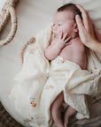 Lifestyle image of a baby swaddled in organic cotton swaddle in Flowers