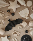 A flat lay of beige and white baby items—including toys, bottles, a pacifier, star-shaped pillows, a black bat toy, and the mushie Star Lovey Blanket—all arranged on a neutral background.