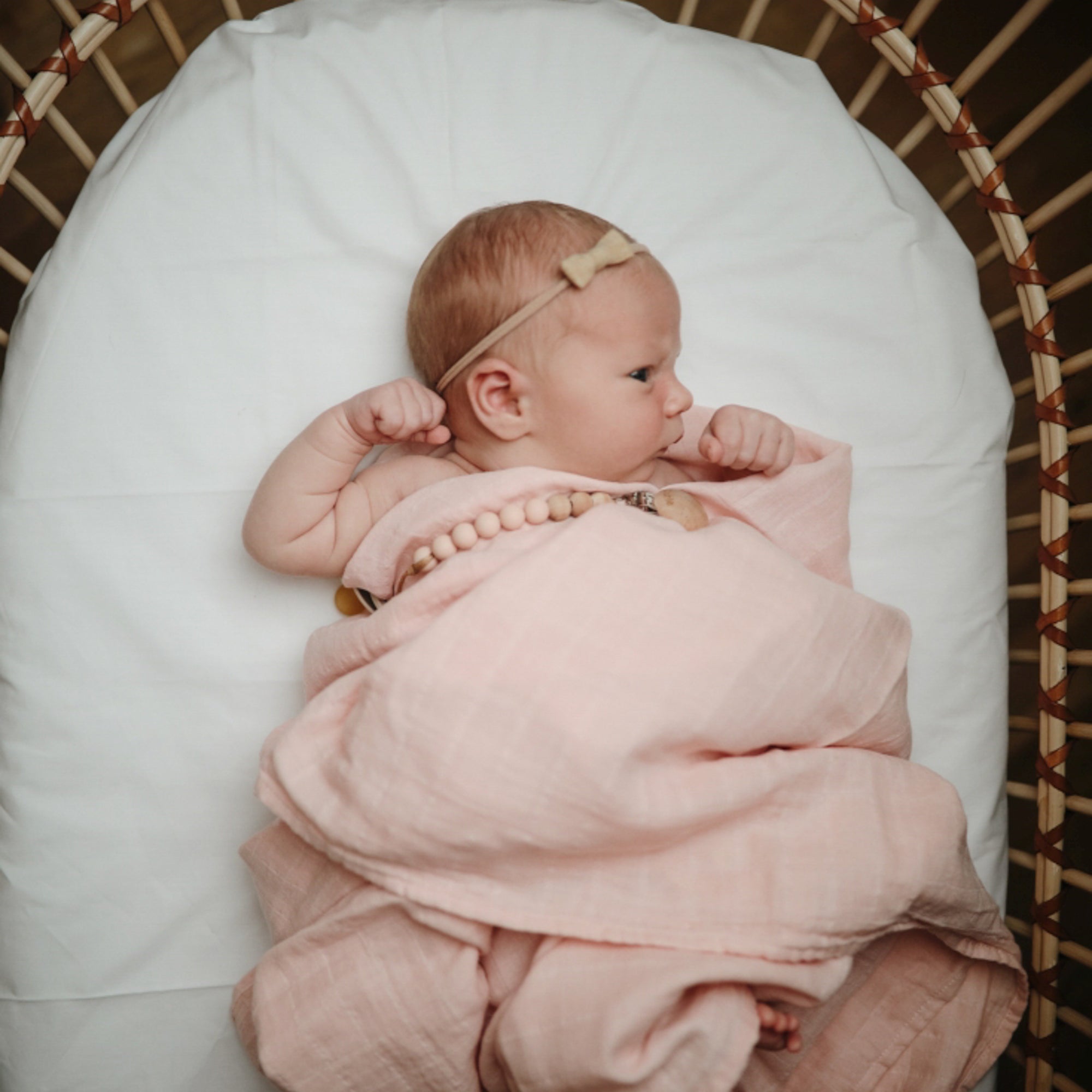 Lifestyle image of a baby swaddled in organic cotton swaddle in Rose Vanilla