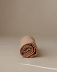 A neatly rolled mushie Multi-Use Cover in light brown stands upright on a smooth beige surface with a neutral background.
