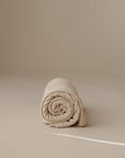 The mushie Multi-Use Cover, shown neatly rolled in beige, rests on a smooth, light surface with a plain, neutral background—ideal for various uses.