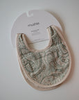 The mushie Muslin Bib, made from organic cotton with a paisley pattern in soft green and cream tones, is shown in its brand packaging against a white background—an ideal, stylish teething bib for little ones.