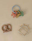 Mushie Teething Gift Set: 3 pastel silicone teethers displayed on a beige background.