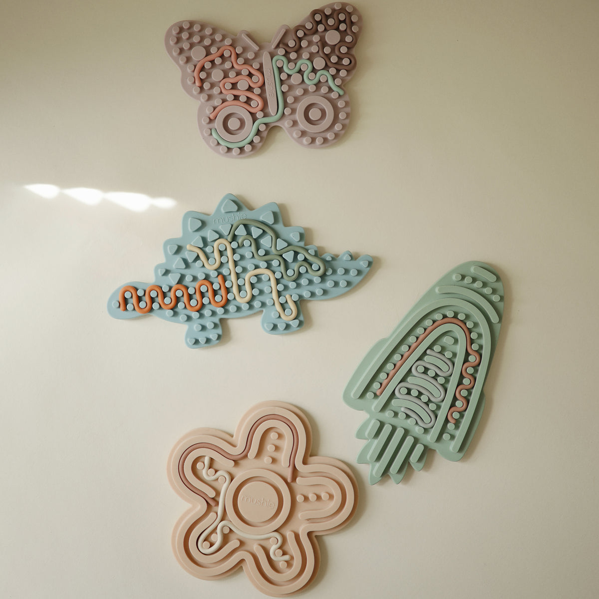 Set of 4 mushie Silicone Sensory Toys: butterfly, dinosaur, rocket, and flower.
