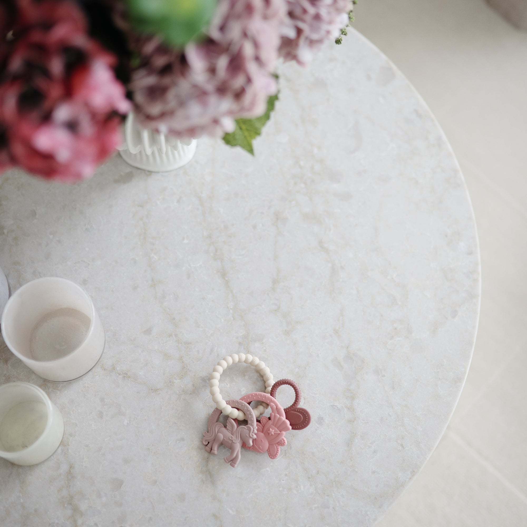 A mushie Fairy Teething Ring with a marble table, floral arrangement, and candles for sensory play.