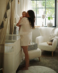 Mother kisses baby in nursery with mushie Diaper Caddy by the crib.