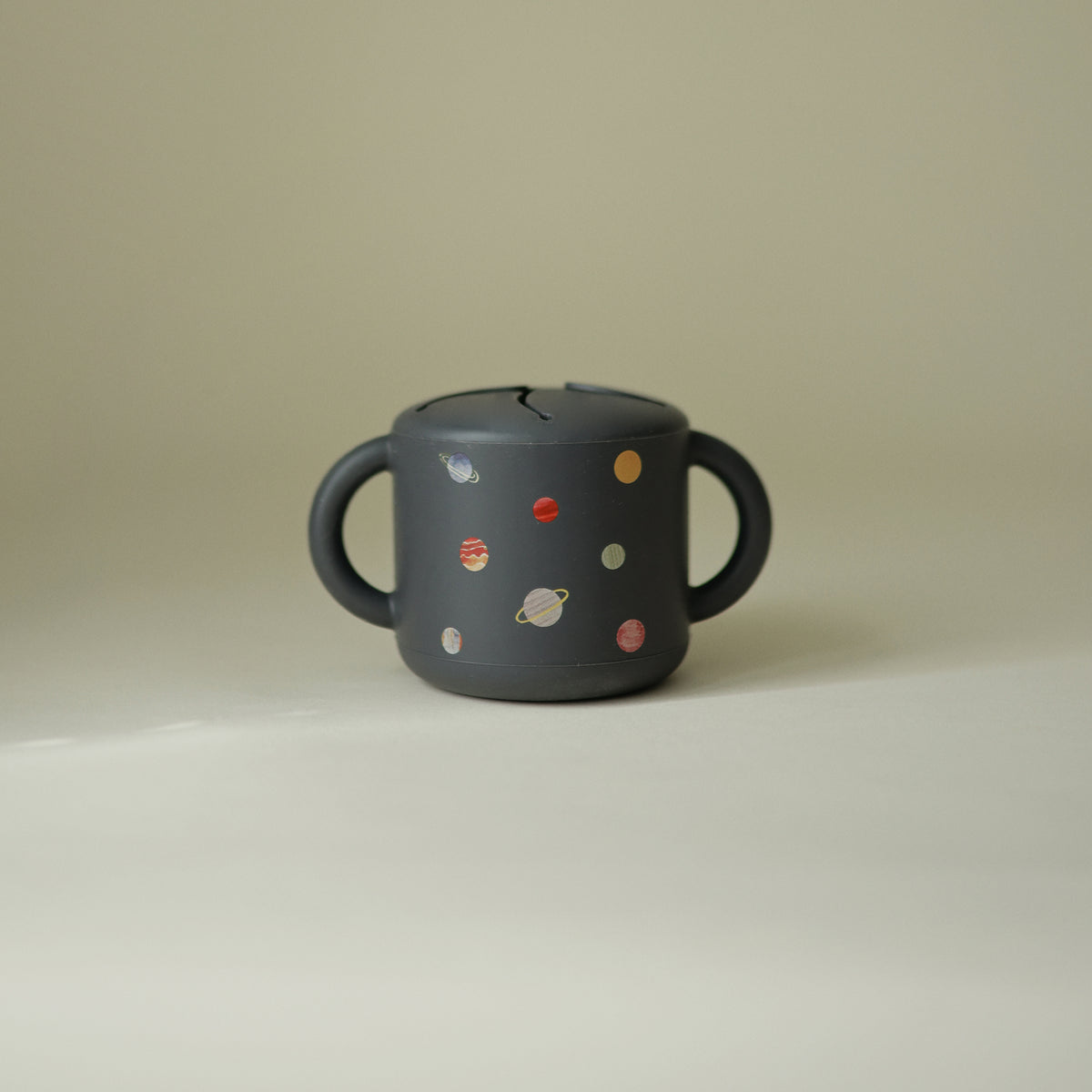 Mushie Snack Cup: Spill-proof silicone, two handles, dark design with planet print for toddlers.
