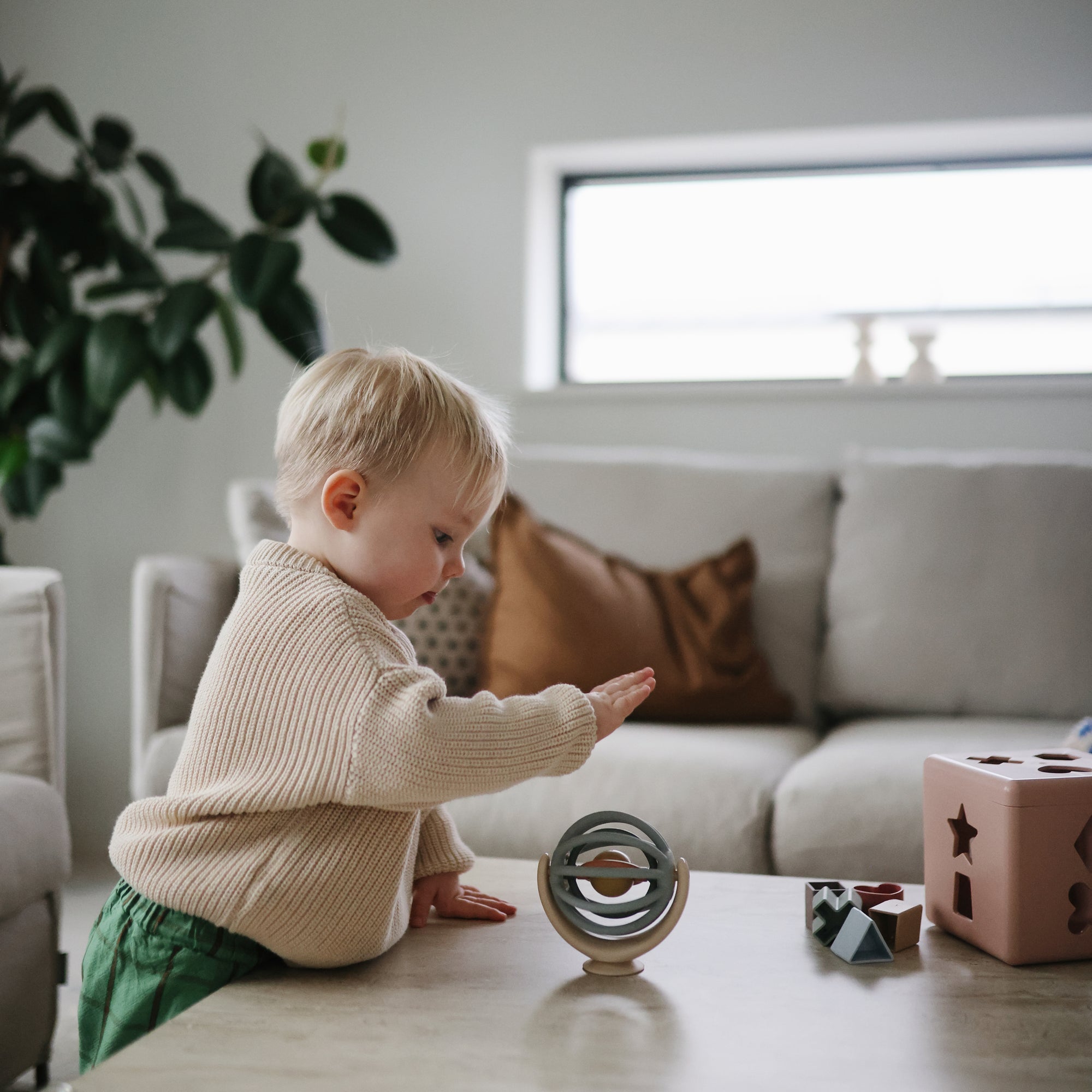 Child playing with mushie sensory toys on a table in a living room