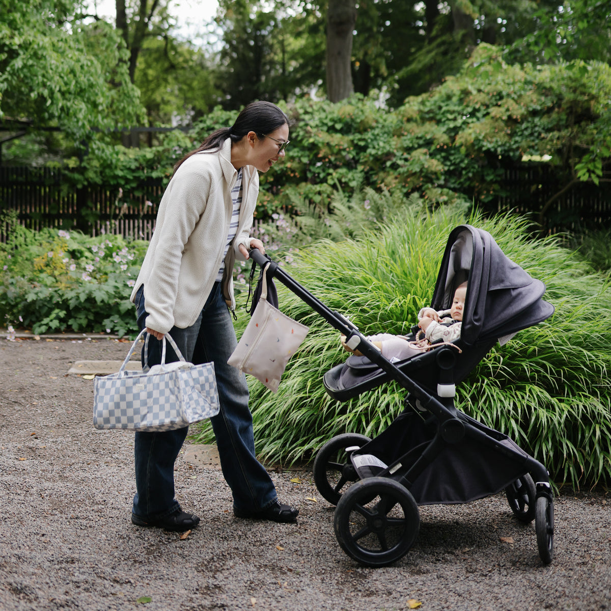 A woman pushes a stroller with a patterned diaper bag and a mushie Water Resistant Wet Bag.