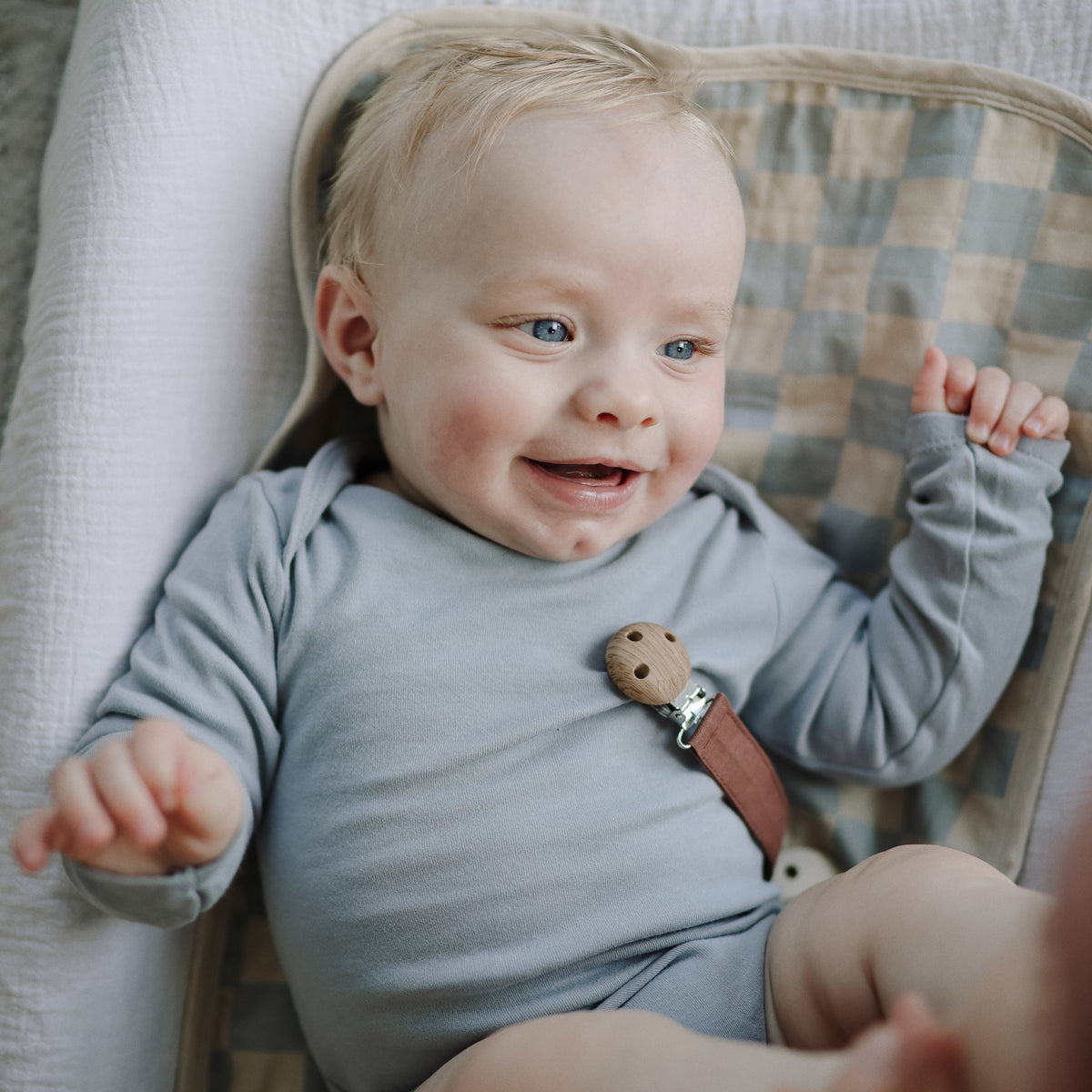 A smiling baby lies on a Mushie Changing Pad Liner.