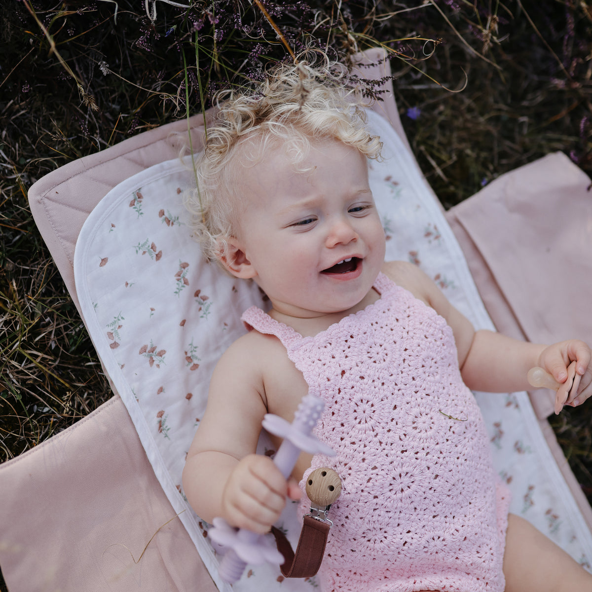 Baby lying on an organic cotton floral Mushie Changing Pad Liner in the grass.