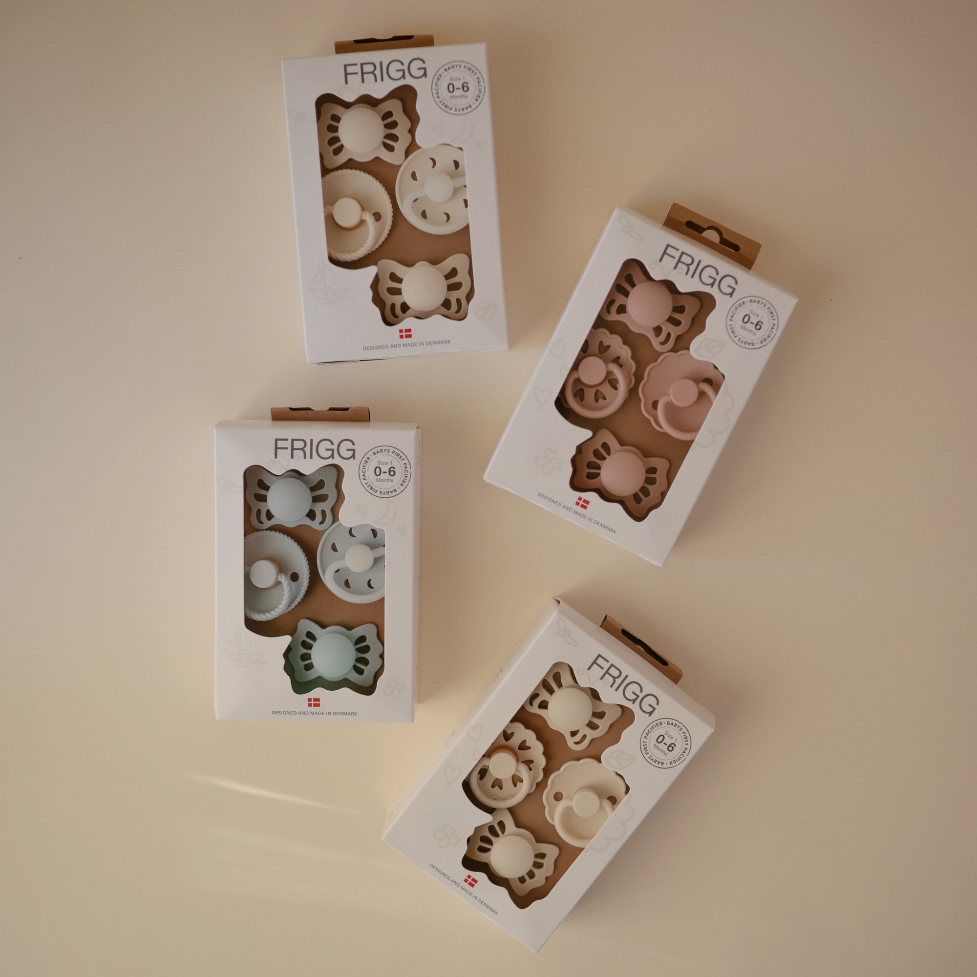 Four boxes of FRIGG Baby's First Pacifier Moonlight Sailing (Cream) 4-Pack are arranged on a neutral surface, each showing two silicone pacifiers for ages 0–6 months with Danish branding.