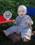 Baby in gingham with mushie Linen Pacifier Clip 2-Pack sits on blue chair by globe outdoors.