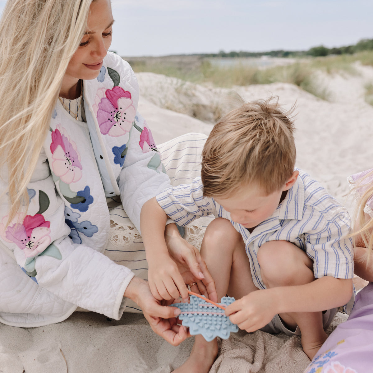 Woman and child on sand, smiling at mushie Silicone Sensory Toy.