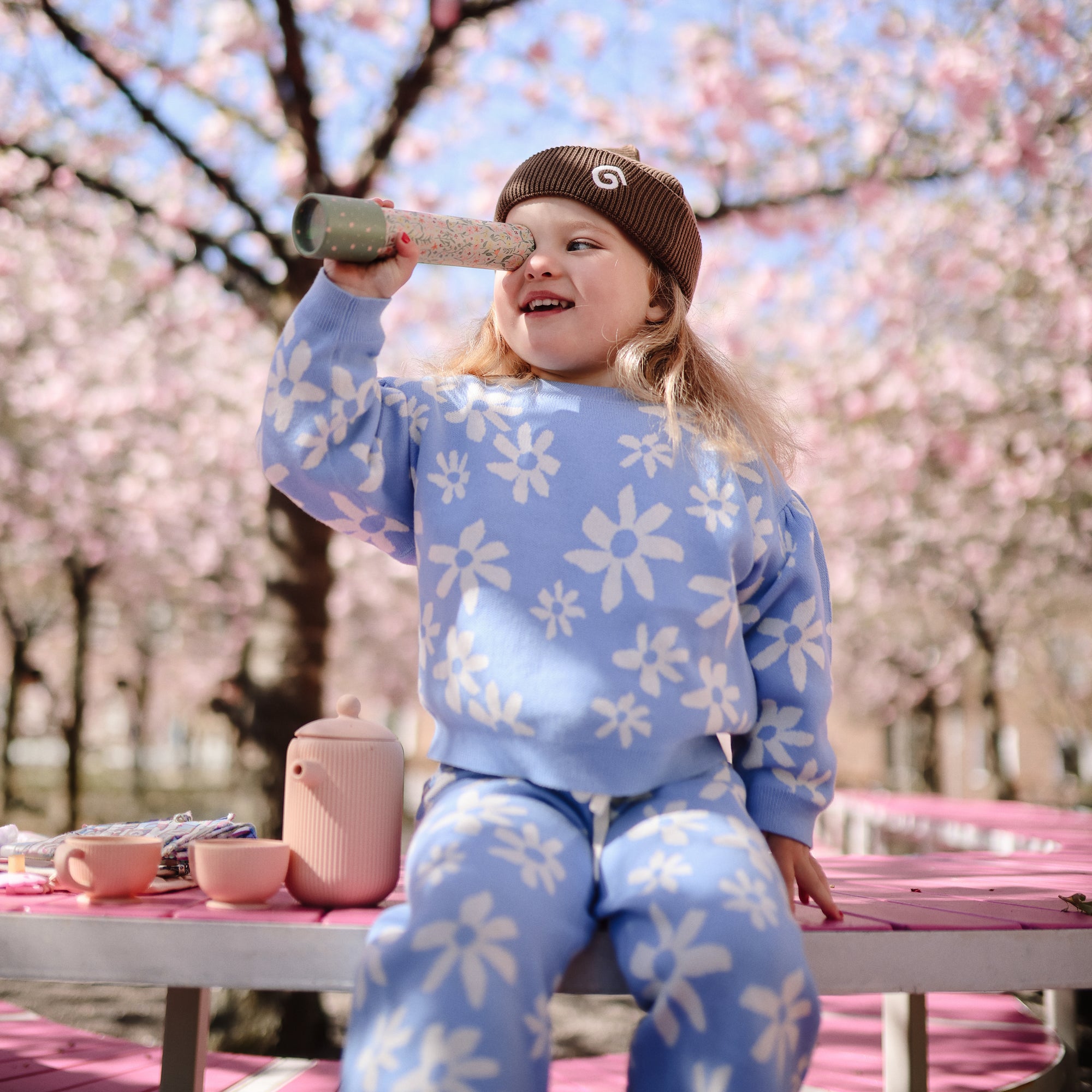 A young child enjoys playing with mushie Kaleidoscopes on a pink outdoor bench.