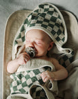 A baby with a pacifier sleeps on Mushie Changing Pad Liners in a checkered hooded towel.