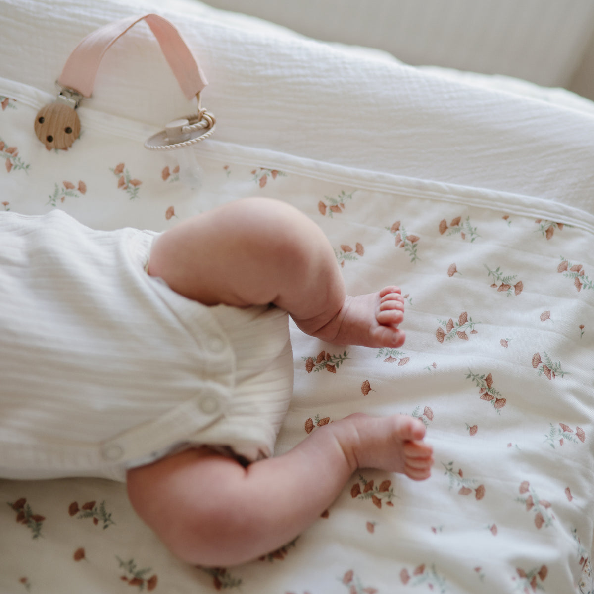 A baby lying on a Mushie floral Changing Pad Liner.