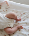 A baby lying on a Mushie floral Changing Pad Liner.