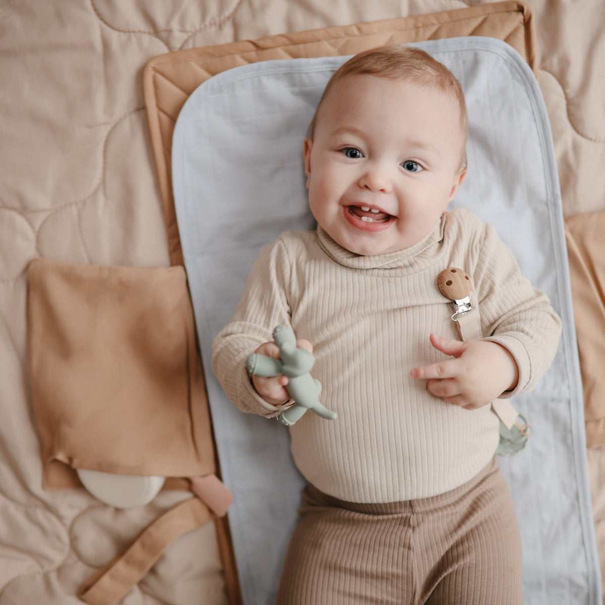 Smiling baby holding a toy while lying on a Mushie Changing Pad Liner.