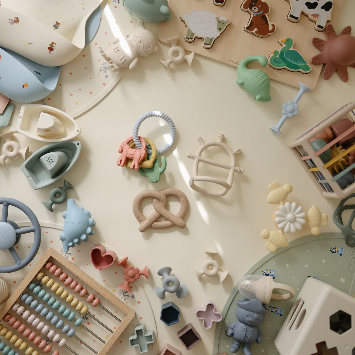 Mushie Teething Gift Set with pastel toys, puzzles &amp; silicone teether on a cream surface.