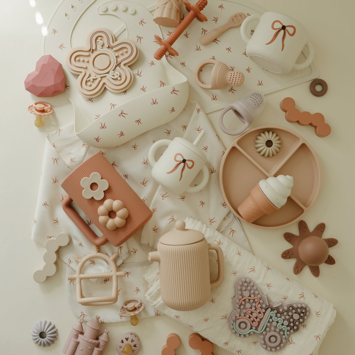 Mushie Snack Cup and pastel toddler toys arranged neatly on a patterned cloth.