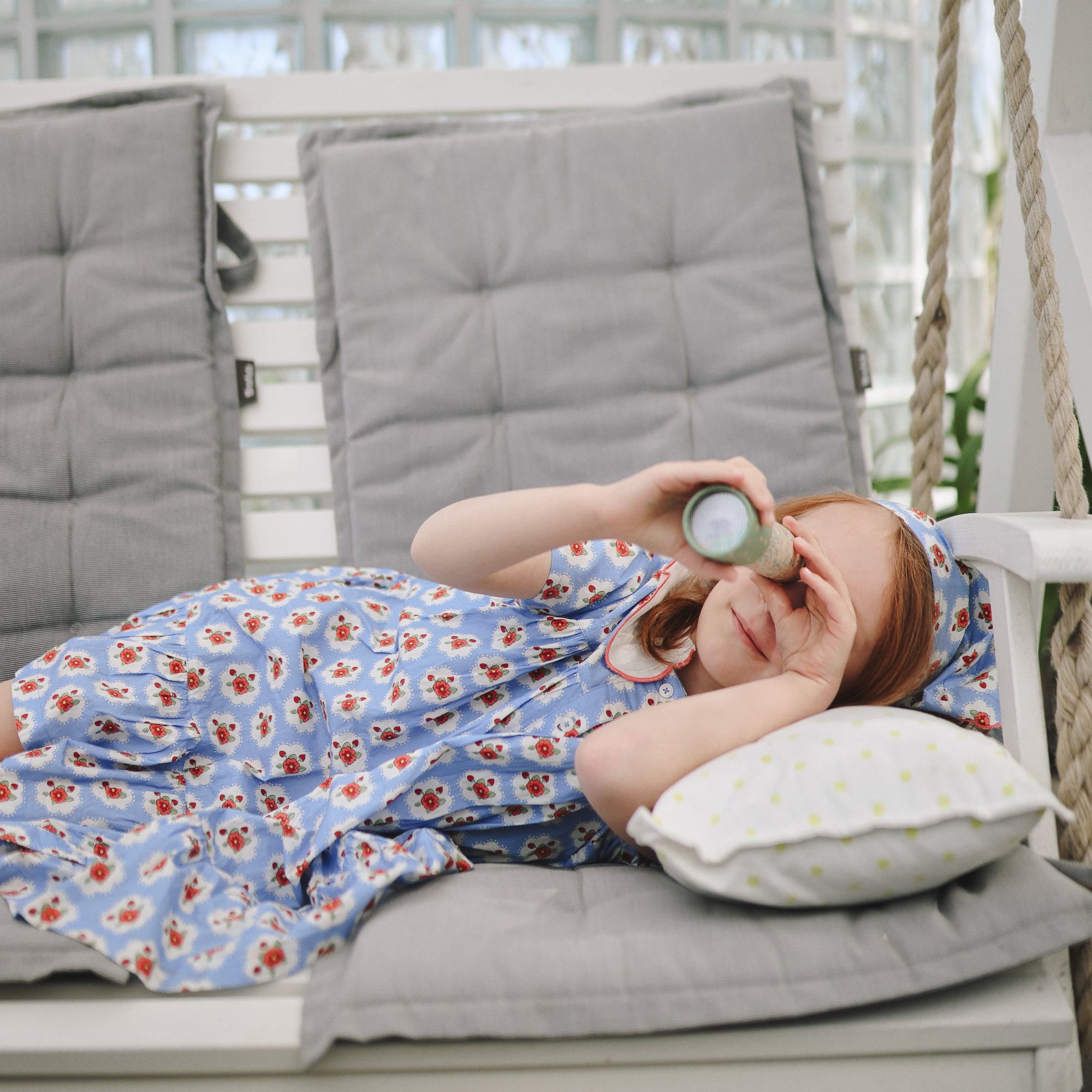 Young girl enjoys imaginative play with mushie Kaleidoscopes while lying on a swing bench.