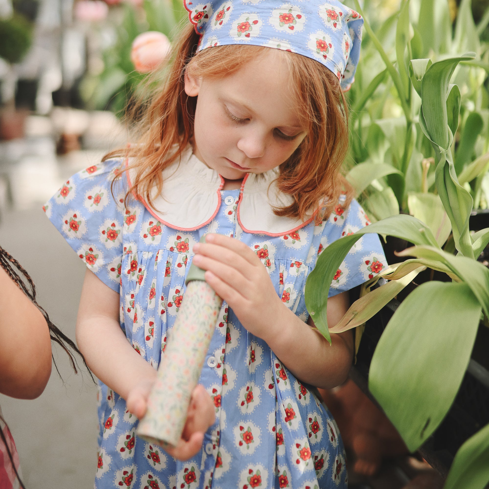 A young girl explores near green plants with a mushie Kaleidoscope.