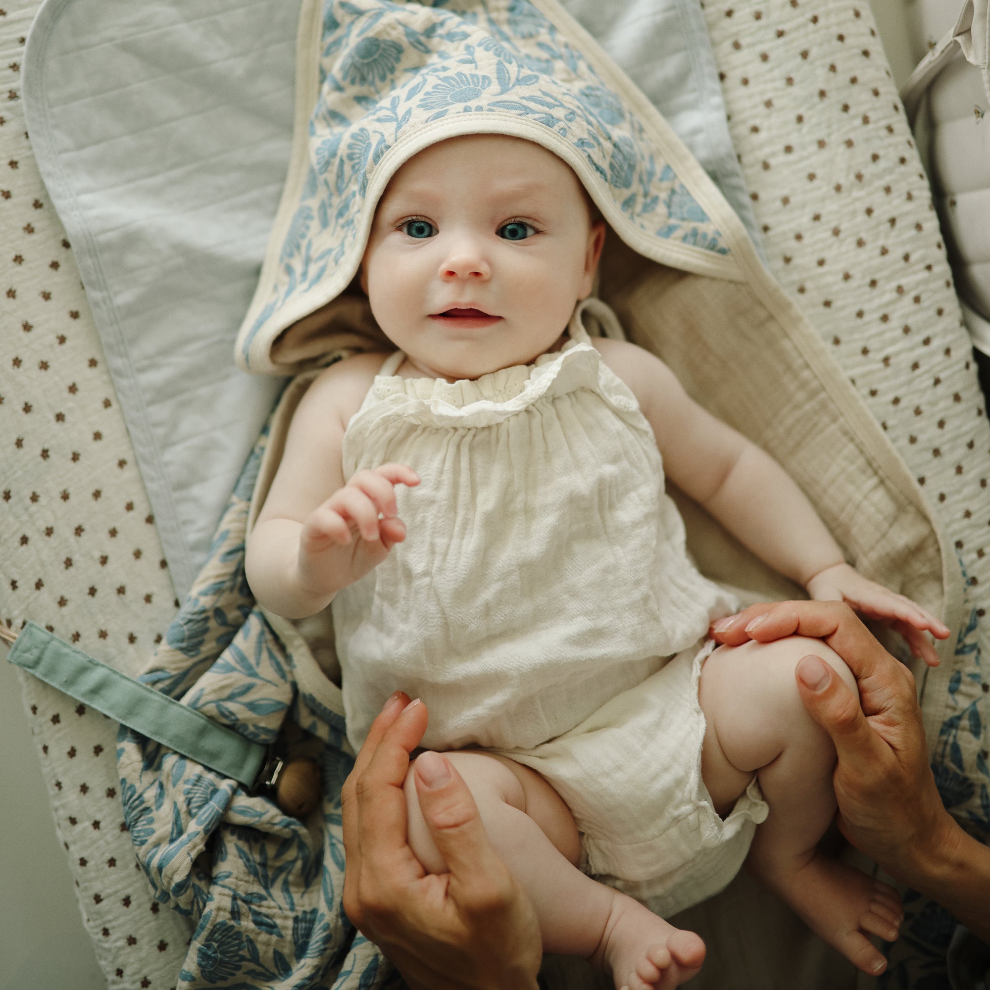 Baby with mushie Linen Pacifier Clip 2-Pack in cream outfit and hooded blanket, gently held.