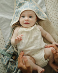 Baby with mushie Linen Pacifier Clip 2-Pack in cream outfit and hooded blanket, gently held.