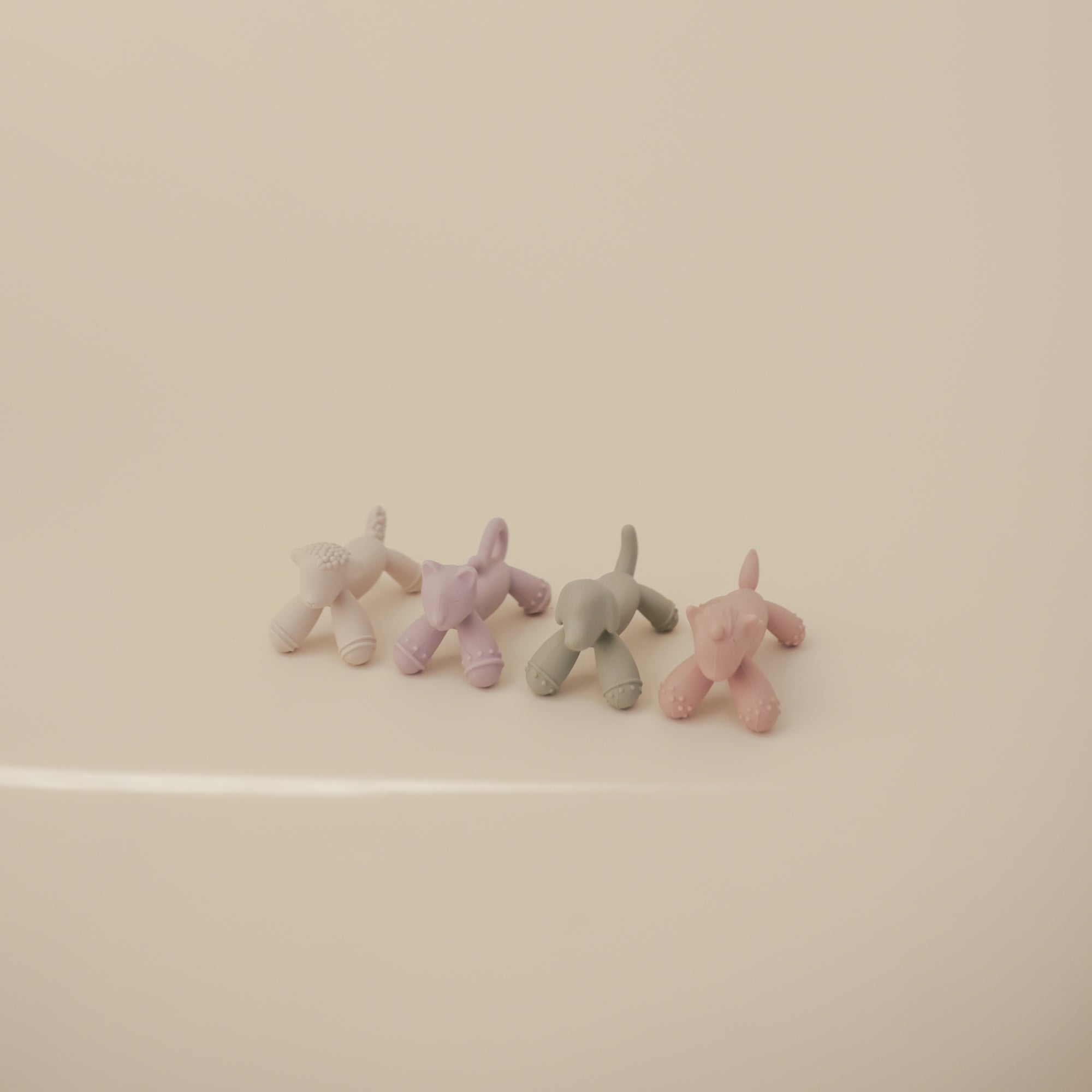 Four small mushie Figurine Teether pastel balloon dogs on a plain, light background.