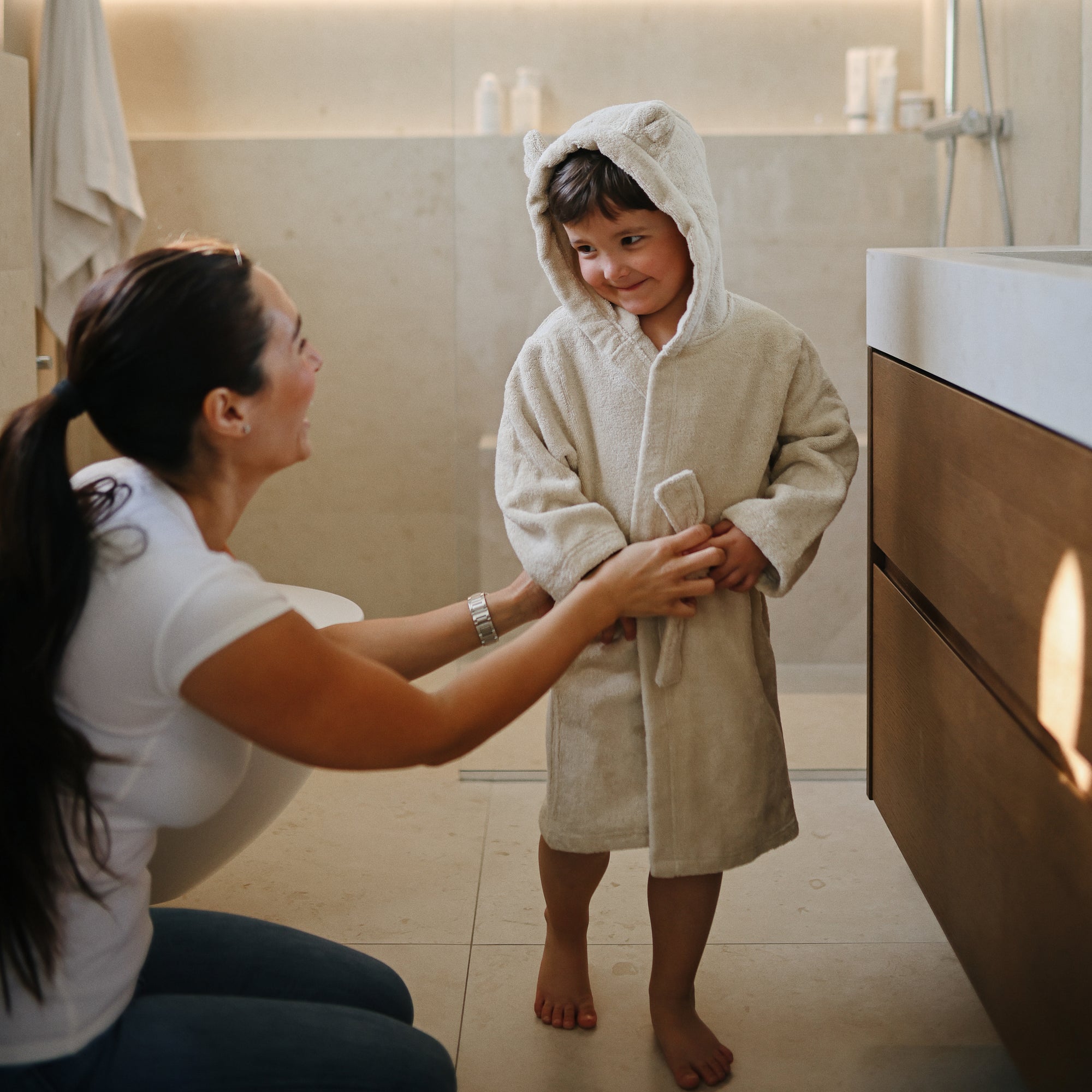 A woman smiles at a child in a mushie Bear Robe in the bathroom.