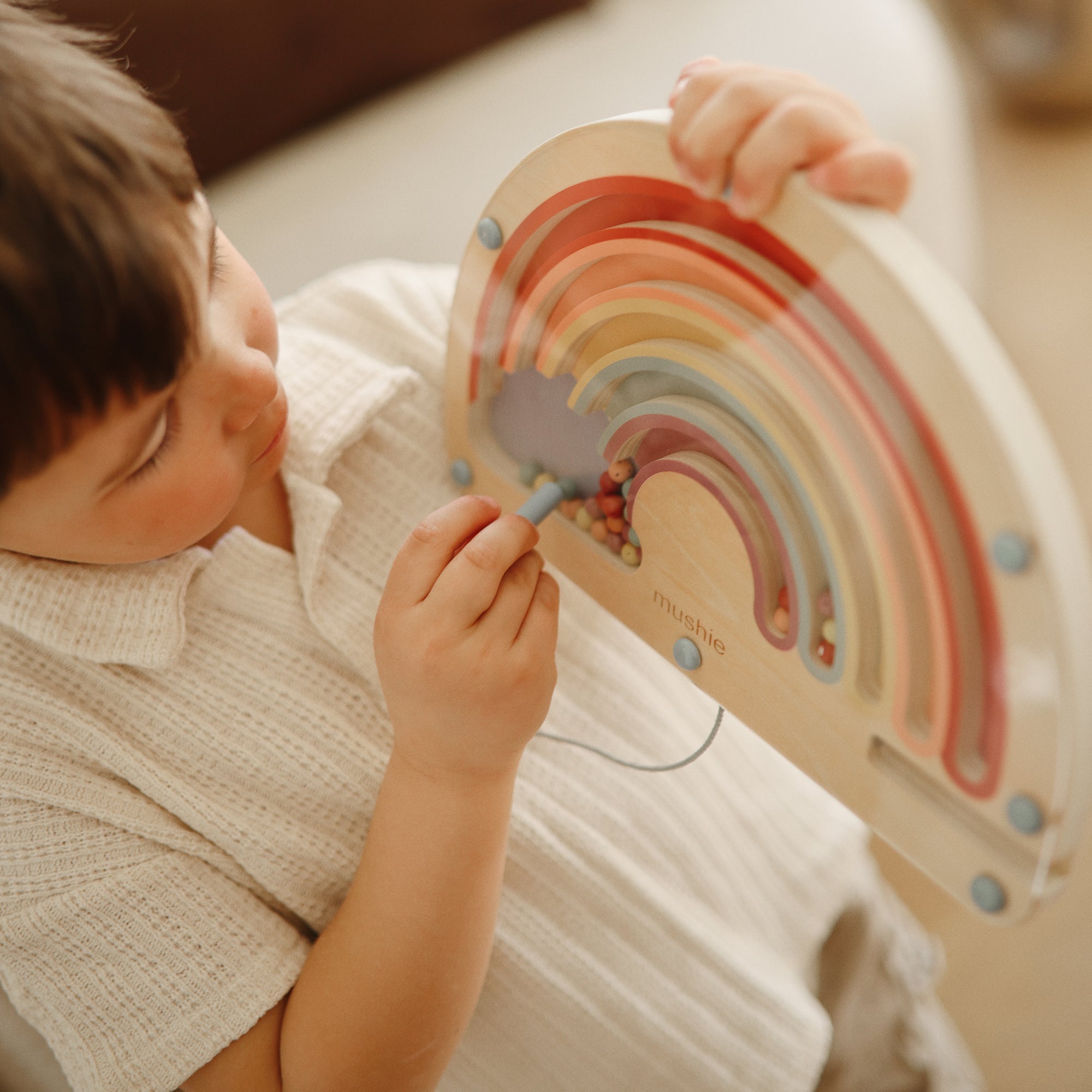 Child enjoys screen-free play with mushie's Wooden Magnetic Rainbow Maze for motor skills.