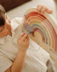 Child enjoys screen-free play with mushie's Wooden Magnetic Rainbow Maze for motor skills.