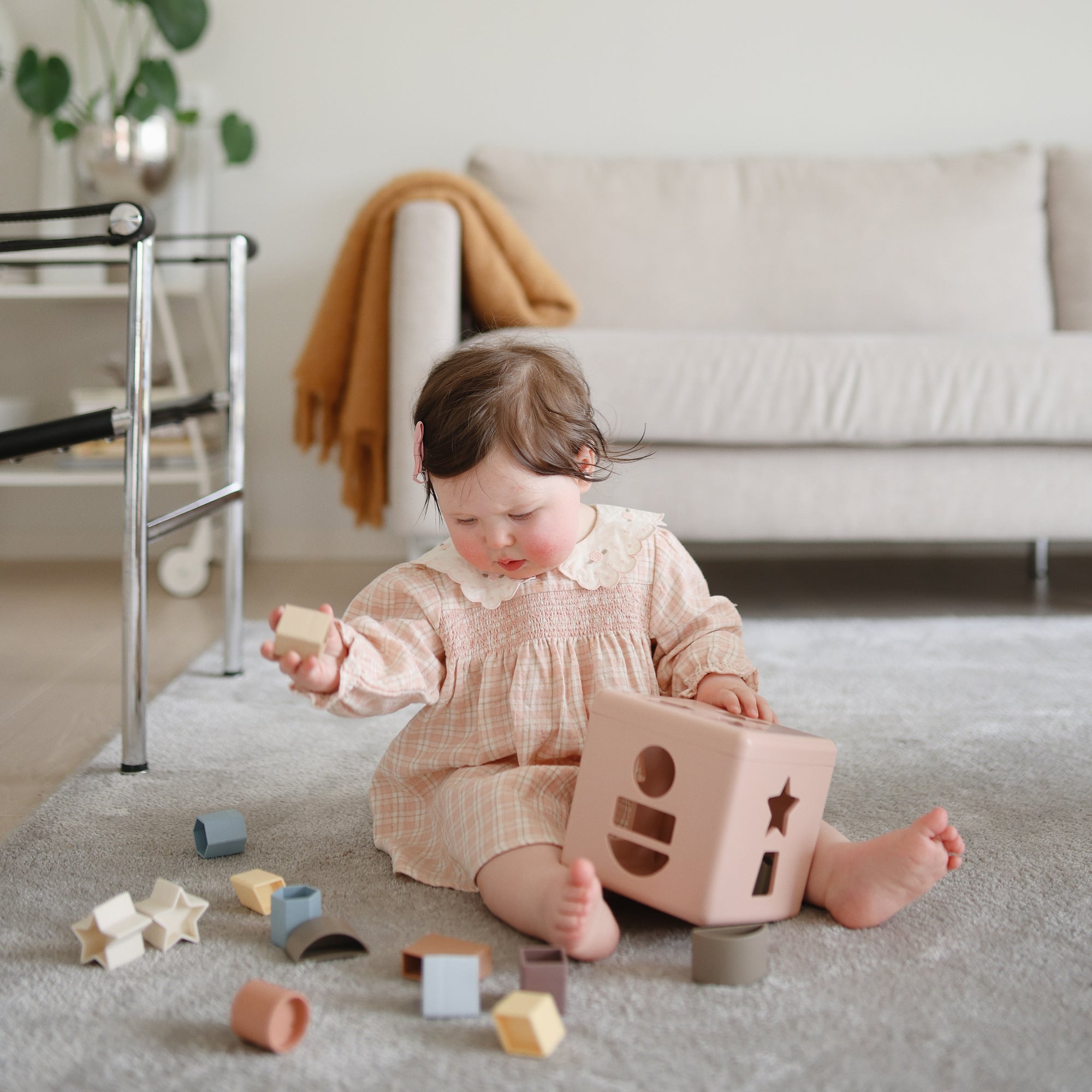 Baby explores the mushie Shape Sorting Box, building fine motor skills on a gray carpet.