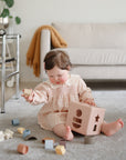 Baby explores the mushie Shape Sorting Box, building fine motor skills on a gray carpet.