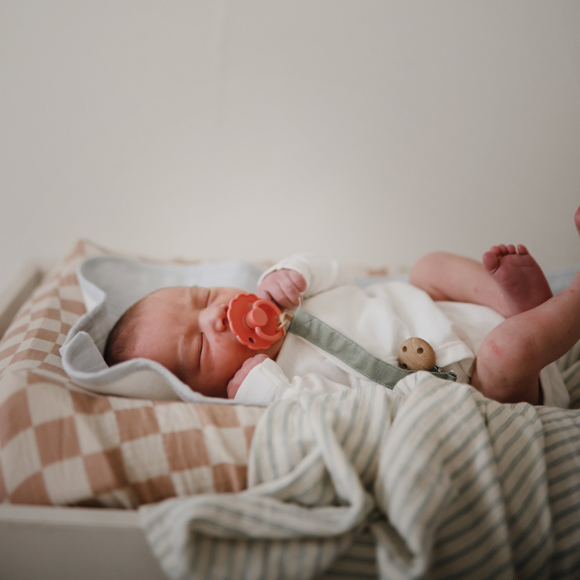 Newborn with pacifier, wrapped in blankets and wearing mushie Linen Pacifier Clip 2-Pack.