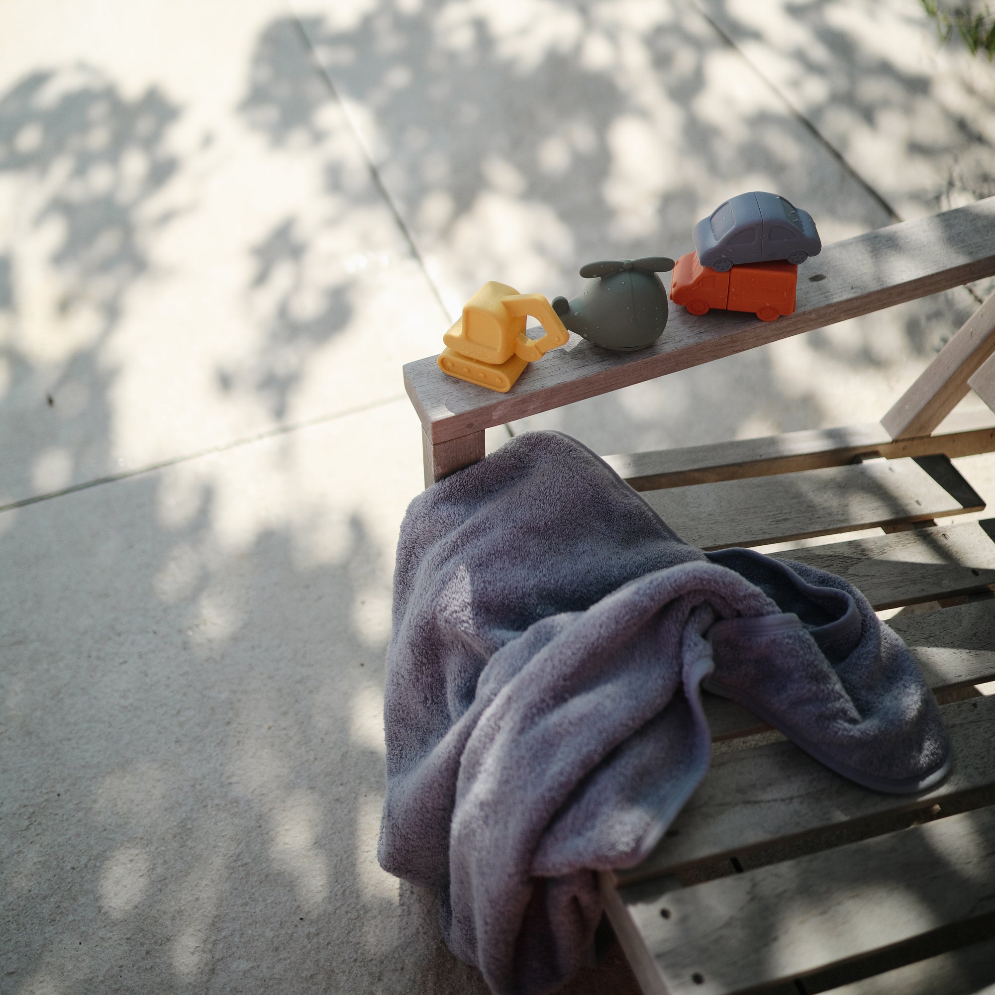 Mushie Mold Free Bath Play Set with food grade silicone toys on a sunlit wooden bench.