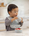Toddler uses Rylee + Cru Feeding Kit Space, eating at the kitchen counter in a silicone bib.