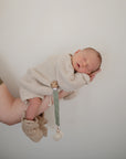 Newborn asleep holding mushie Linen Pacifier Clip 2-Pack against a plain background.