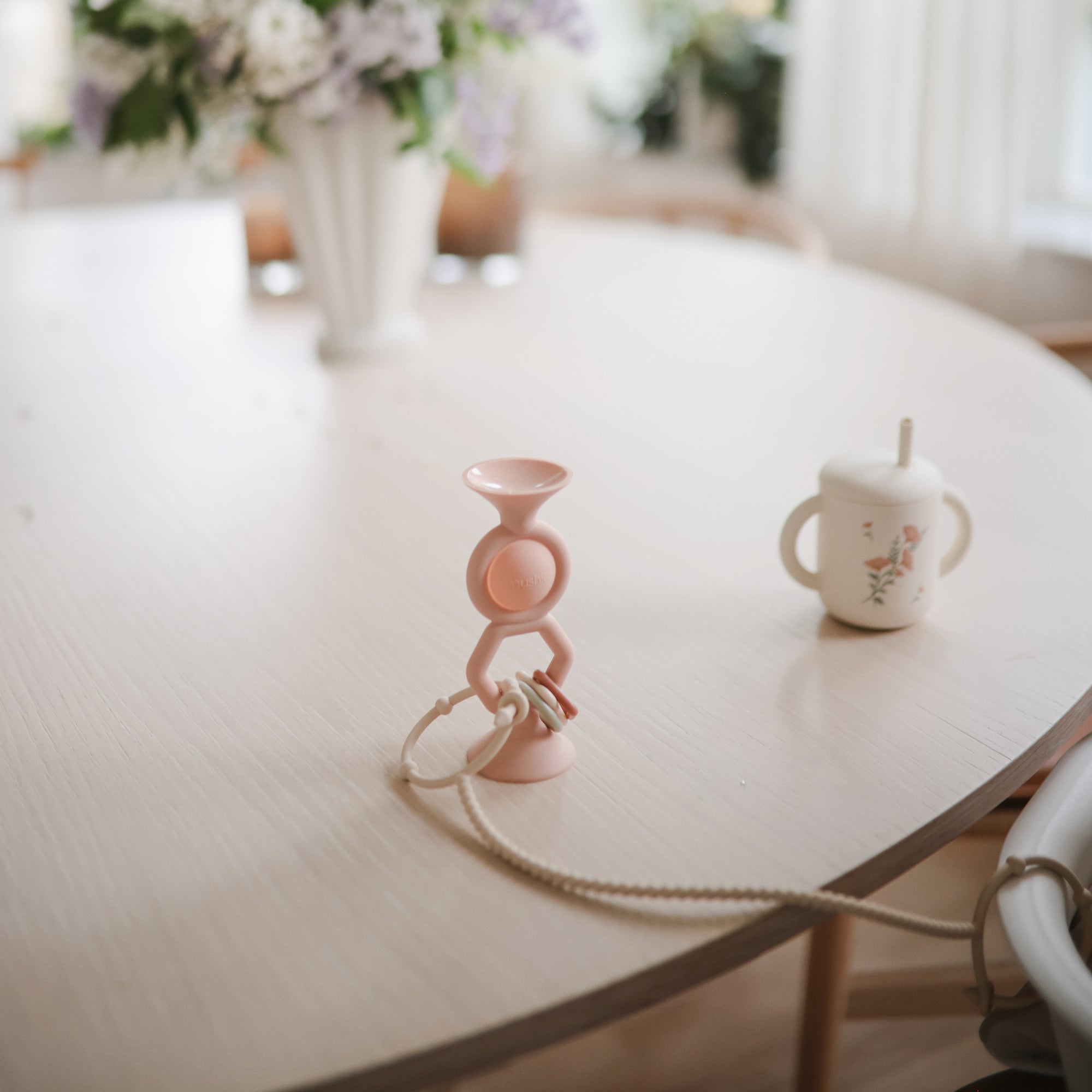 Mushie HexaPop Suction Toy and sippy cup on a table, with flowers in the background.