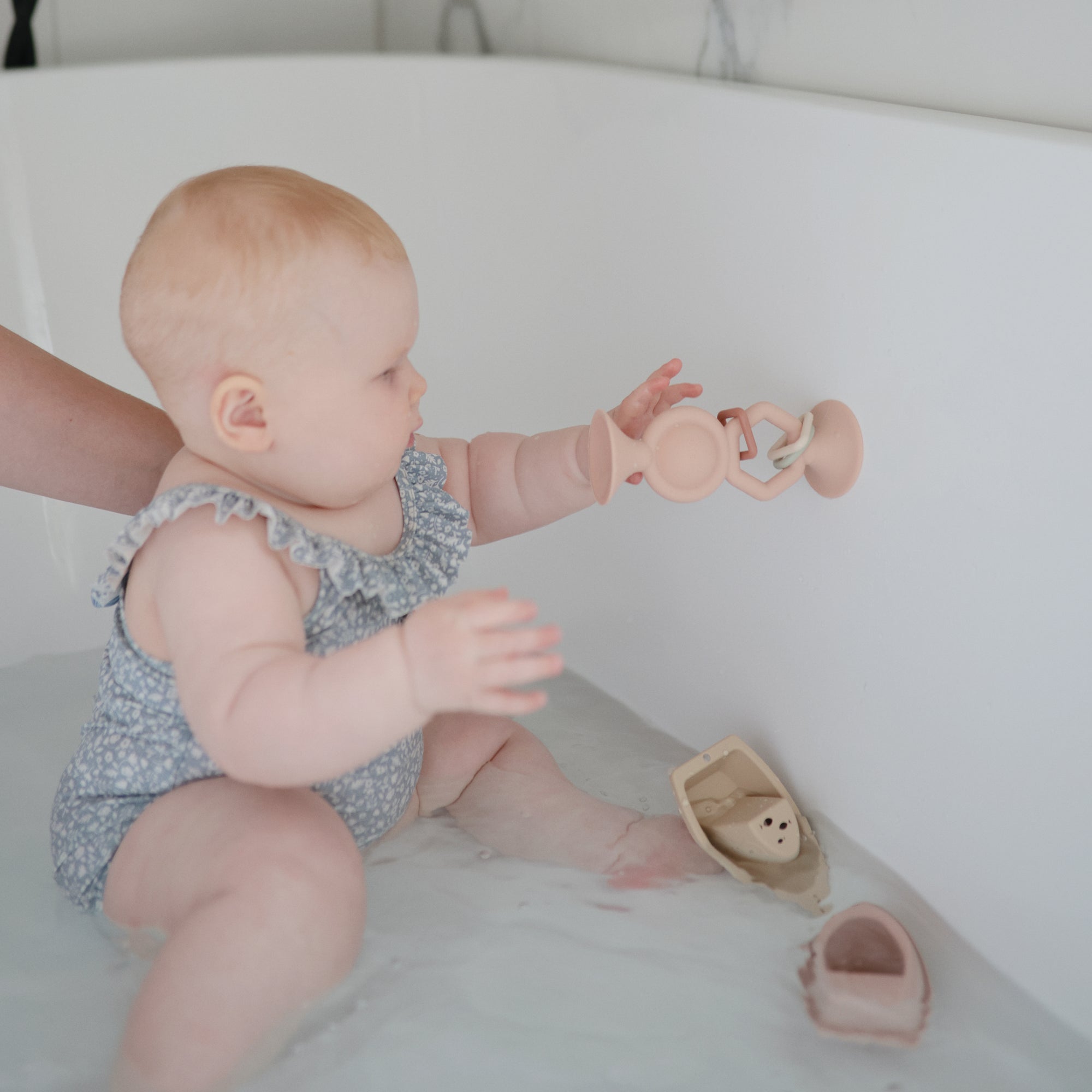 Baby in bath reaches for mushie HexaPop Suction Toy, with sensory toys close by.