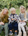Three kids smile outdoors, playing with mushie’s Silicone Sensory Toy for fine motor fun.