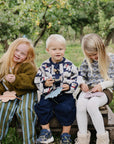Three young children smile outdoors, playing with mushie Silicone Sensory Toy fine motor crafts.