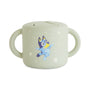 The mushie Bluey x Mushie Snack Cup features a light green color, two handles, a flexible lid, and a playful Bluey dog surrounded by white stars—perfect for your baby feeding essentials.