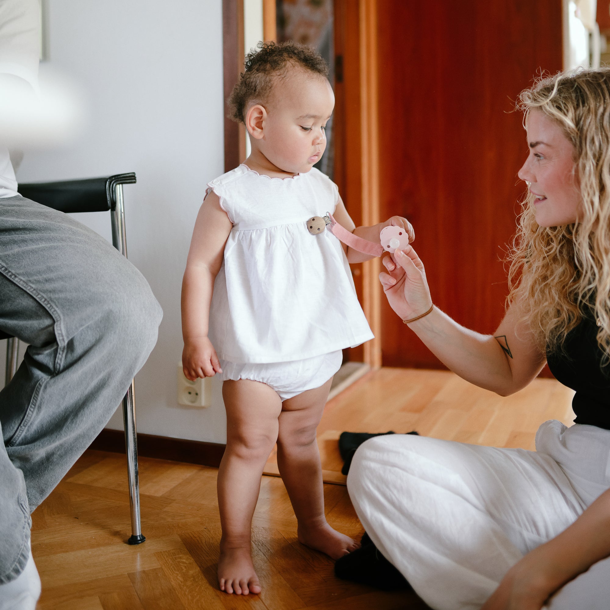 A woman shows a toy to a toddler near mushie Linen Pacifier Clip 2-Pack indoors.