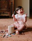 Smiling baby on a rug, playing with mushie Teething Ring and colored chalk.