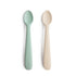 Two mushie Silicone Feeding Spoons, in mint green and beige, lie side by side on a white background. The brand name "mushie" is embossed on each handle.