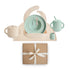 The mushie Deluxe Vanilla Confetti/Cambridge Blue Feeding Kit includes a speckled silicone bib, plate, spoon, fork, handled cup, sippy cup, and small container—all toddler feeding essentials in soft pastels presented as a perfect gift.