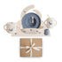 The mushie Deluxe Whales/Tradewinds Feeding Kit includes a blue plate, spoon, fork, two-handled mug, spill-proof cup, and whale placemat neatly arranged above a brown gift box tied with a white ribbon.